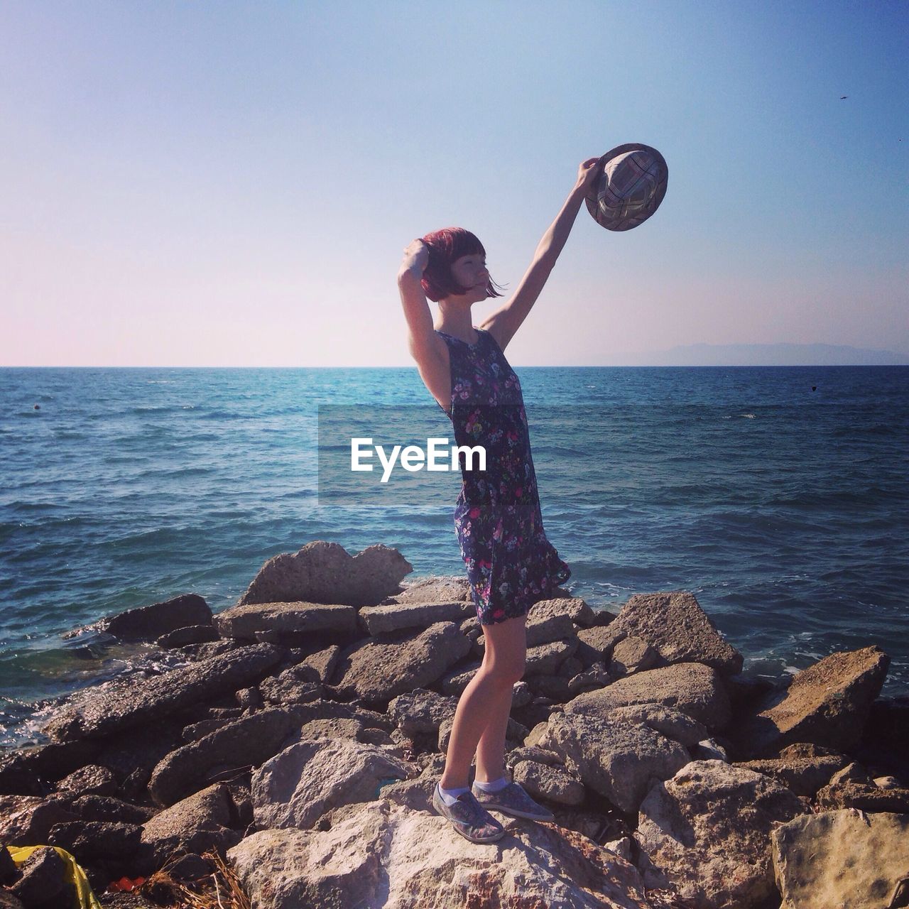 Woman with hat standing on rocks against sea and sky during sunny day