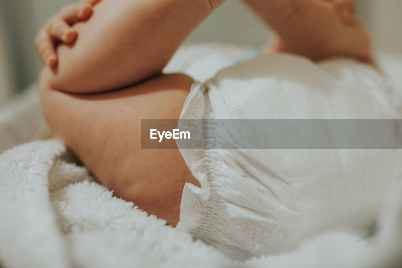 Low section of baby sleeping with feet up on bed