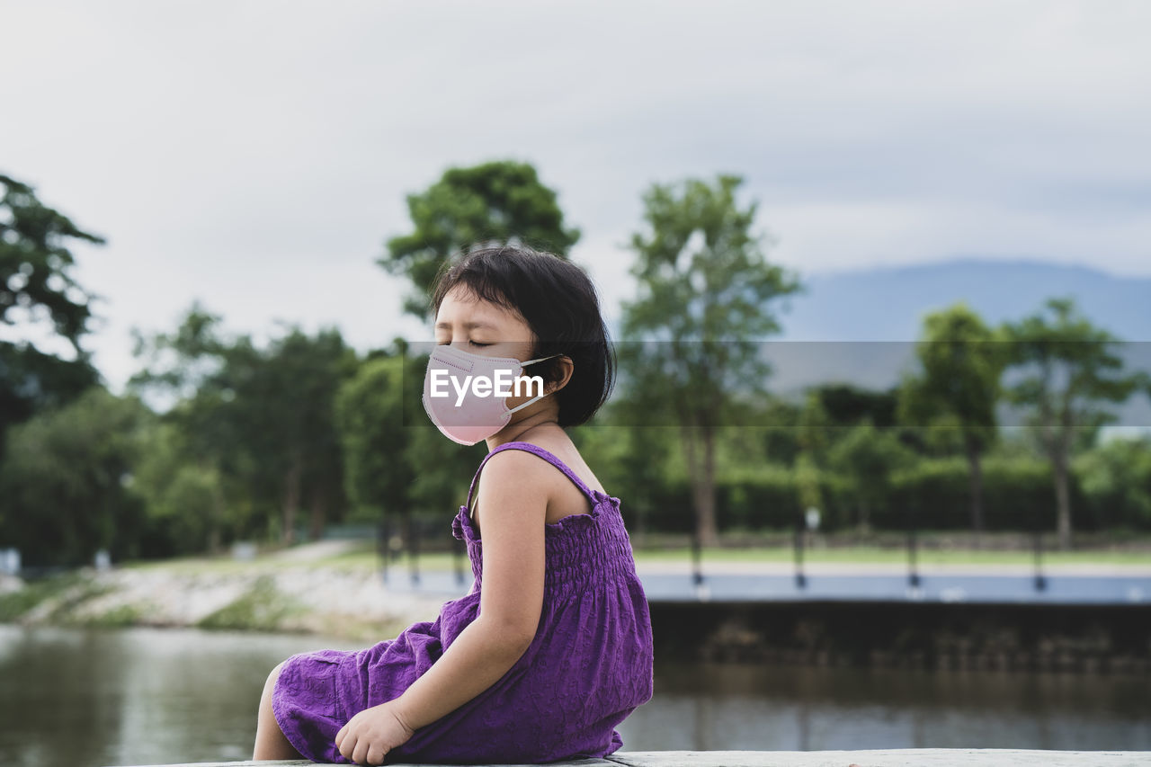 Woman sitting on purple tree by lake against sky