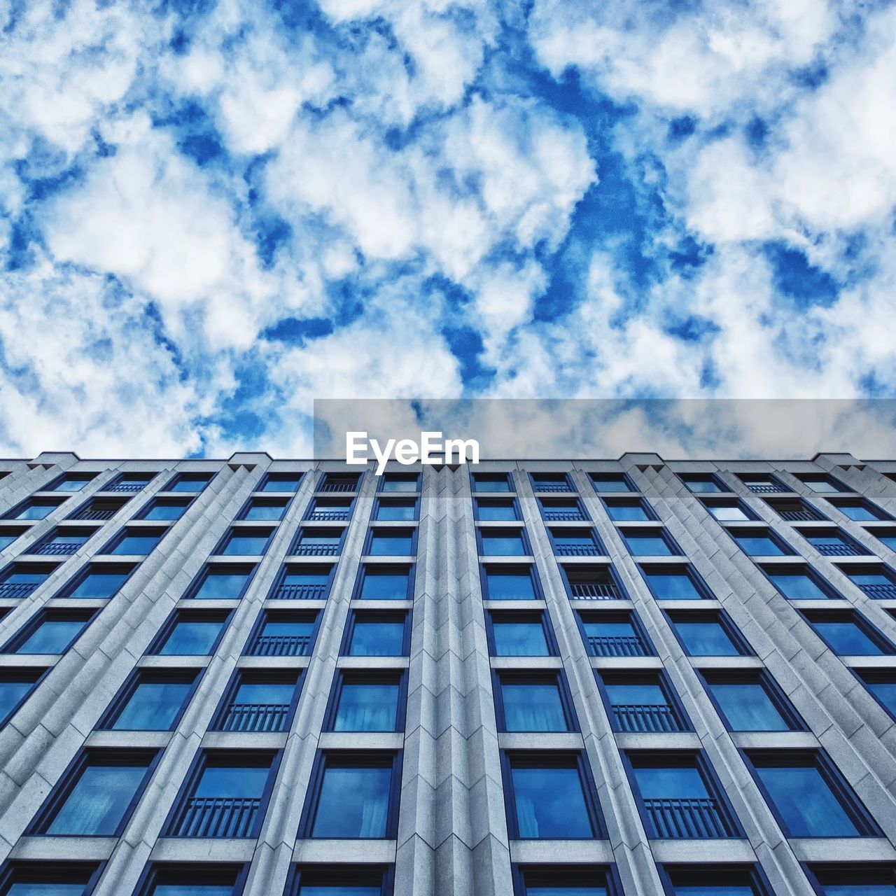 Low angle view of blue glass window building against cloudy sky