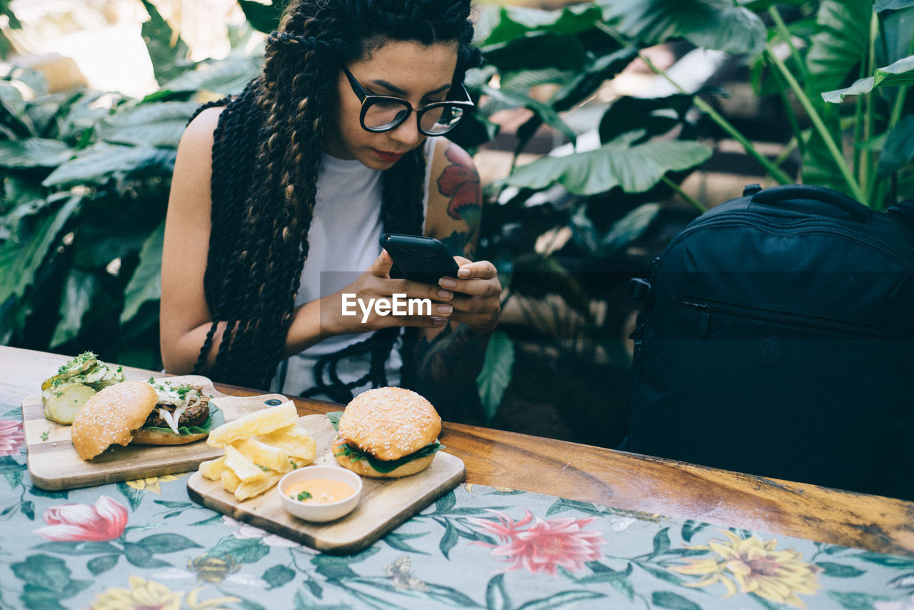 Woman using mobile phone while sitting by food on table