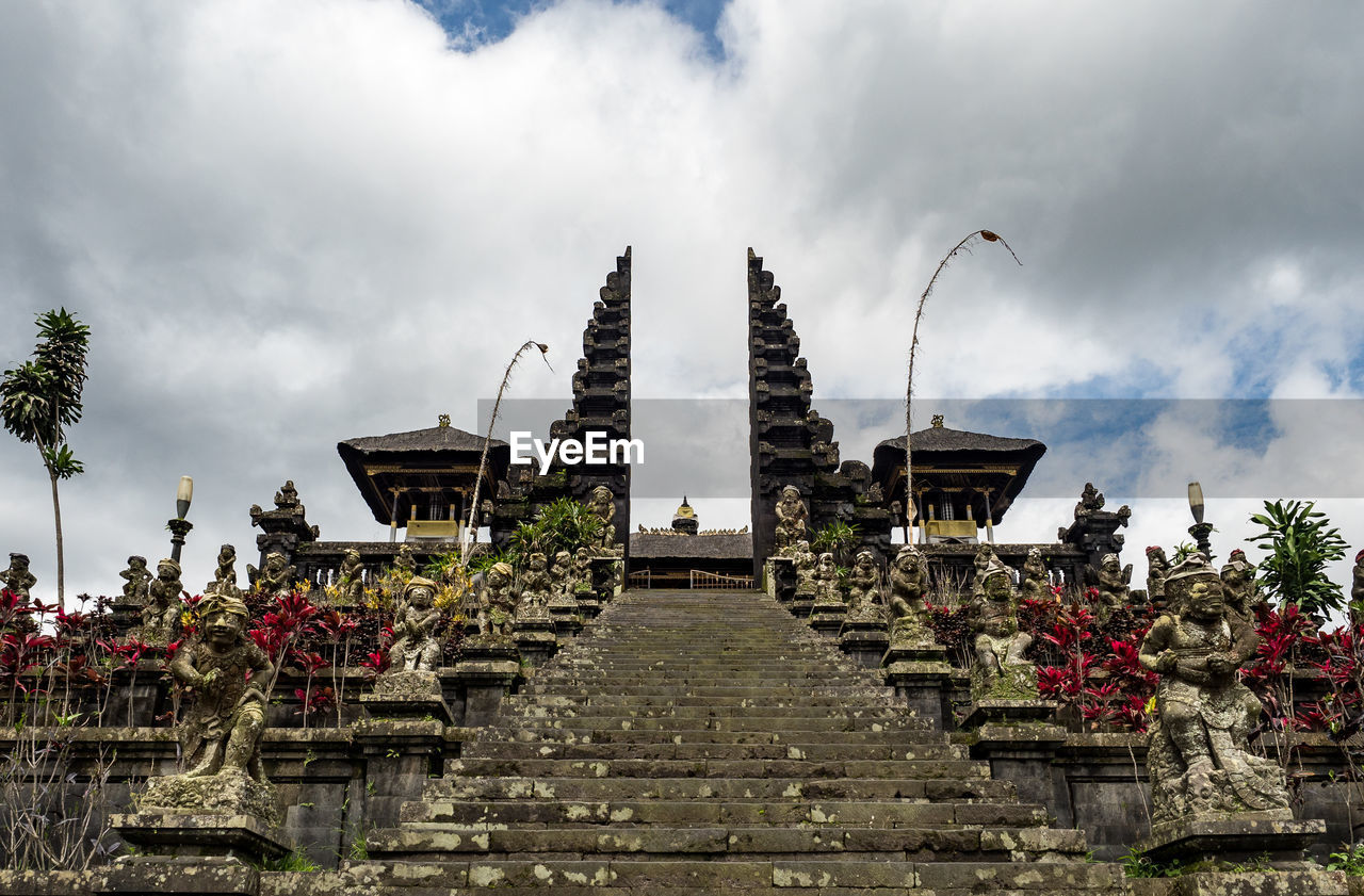 Low angle view of steps amidst statues against cloudy sky