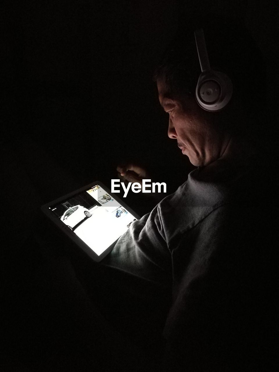 Side view of mature man using digital tablet while sitting in darkroom at home