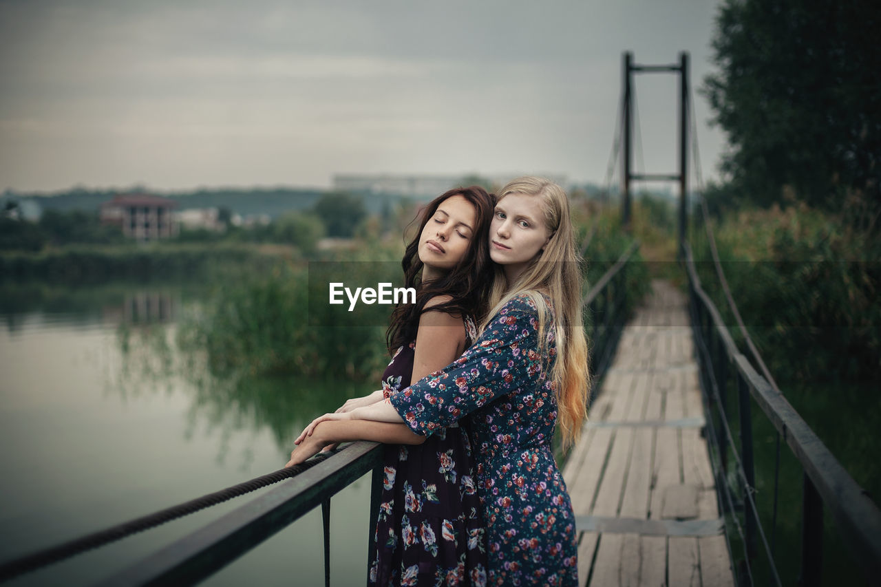 Lesbian couple embracing on footbridge against sky