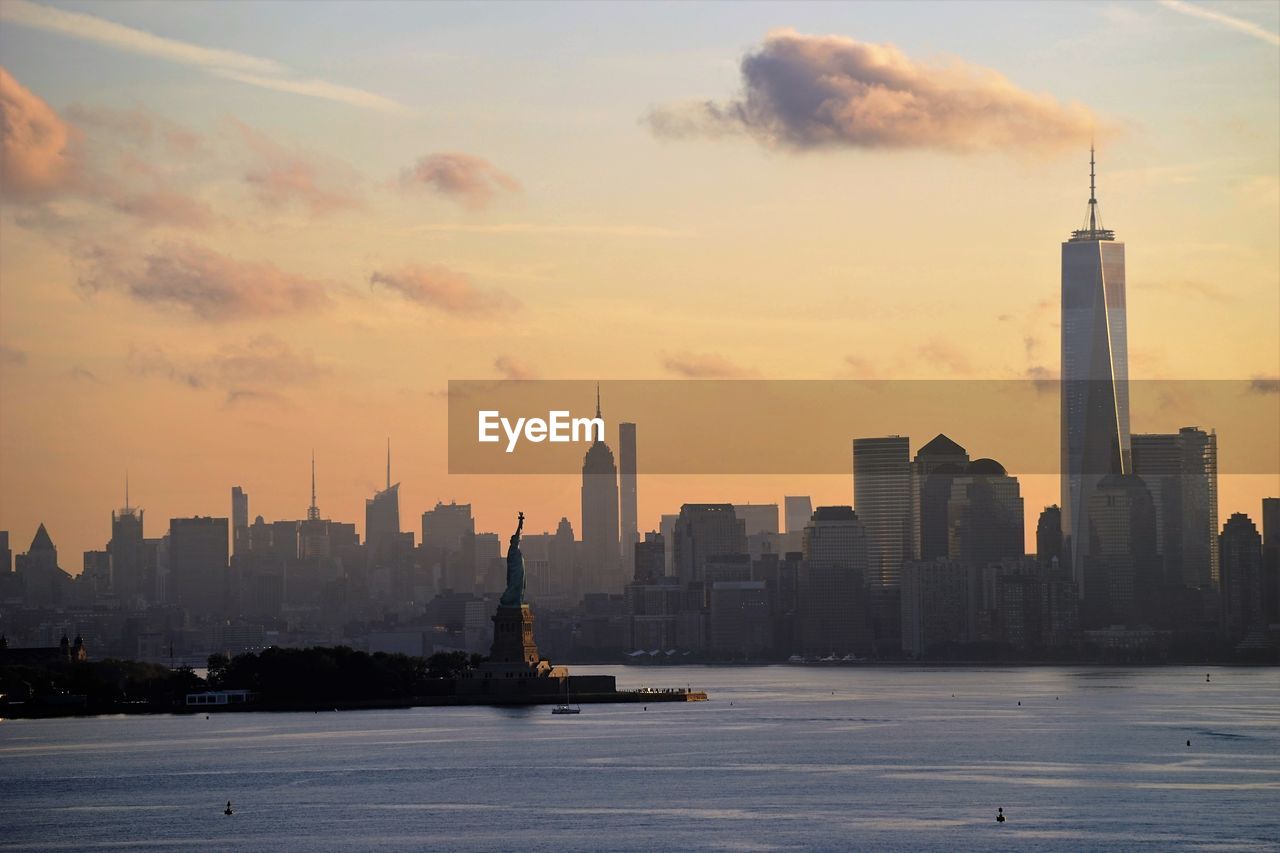 Statue of liberty and manhattan skyline against sky during sunset