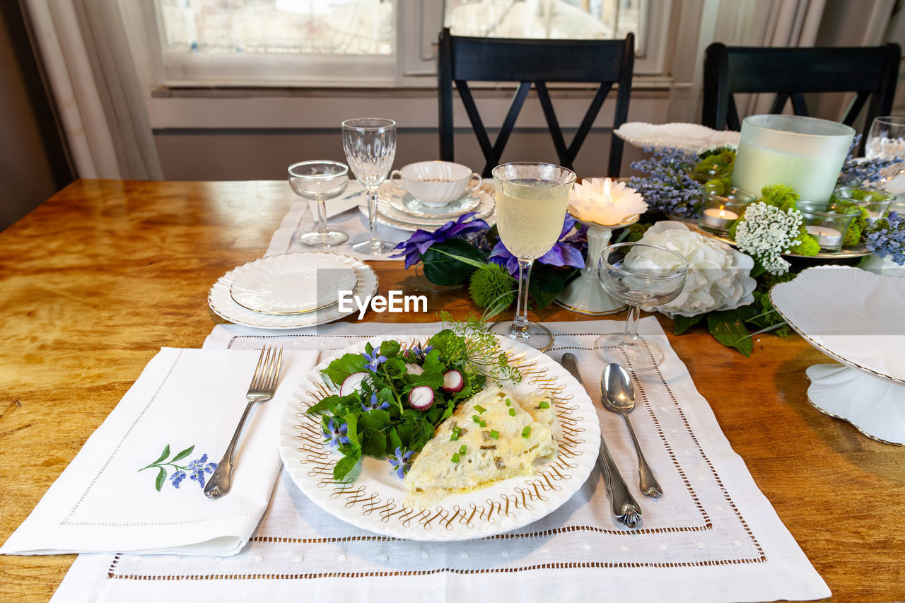 table, food and drink, plate, food, glass, place setting, setting, furniture, meal, dining table, indoors, eating utensil, fork, household equipment, freshness, drinking glass, flower, healthy eating, no people, chair, kitchen utensil, flowering plant, napkin, plant, tablecloth, wine glass, crockery, drink, arrangement, home interior, seat, dining room, knife, high angle view, dinner, domestic room, vegetable, wellbeing, brunch, nature, domestic life, table knife, lunch, elegance, restaurant, candle, celebration, still life, refreshment, lifestyles, flower arrangement, decoration, wood, salad