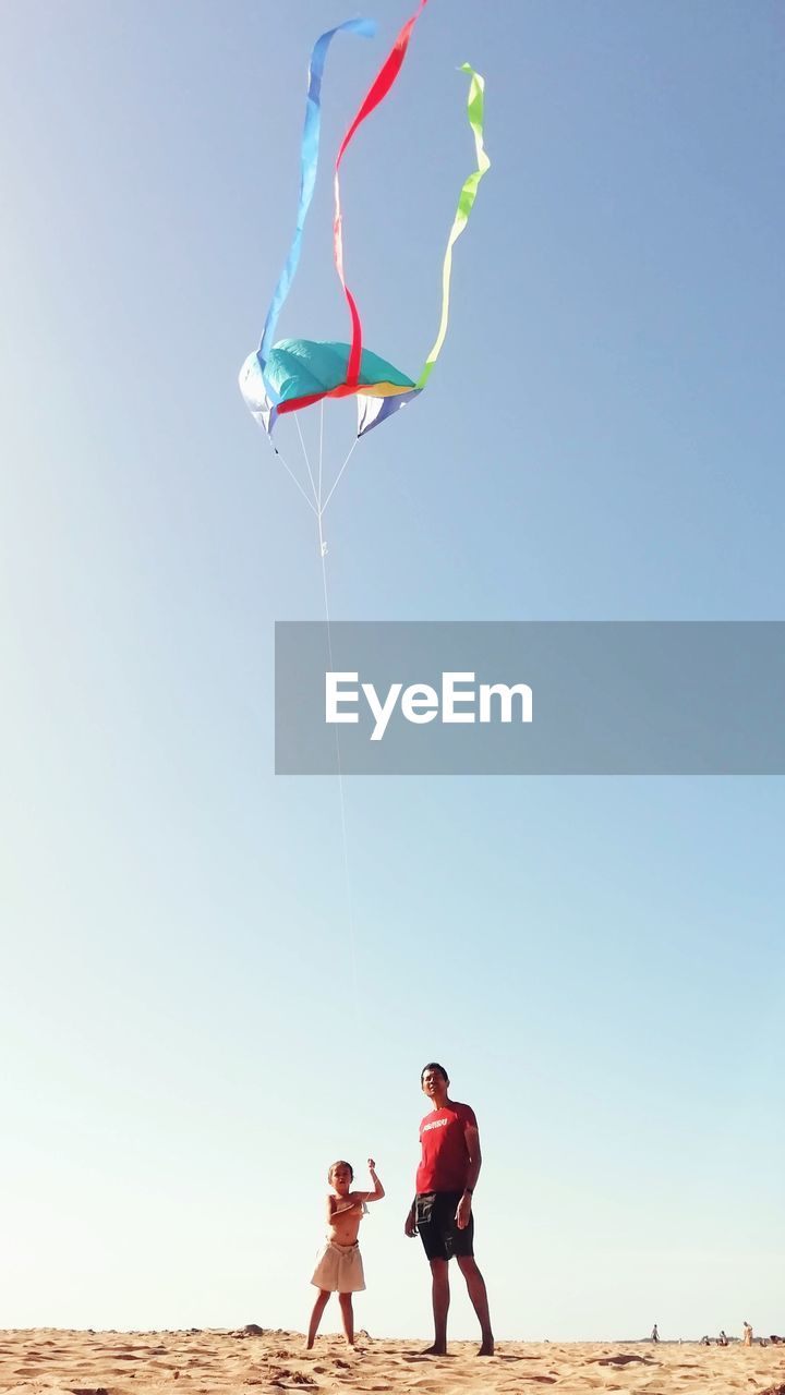 FULL LENGTH OF FRIENDS FLYING KITE ON BEACH