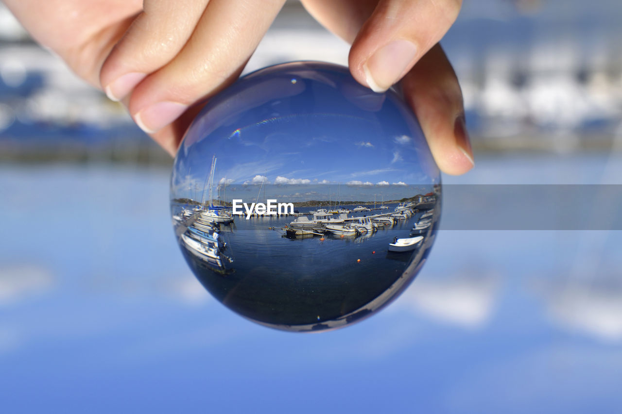 Upside down image of hand holding crystal ball at harbor