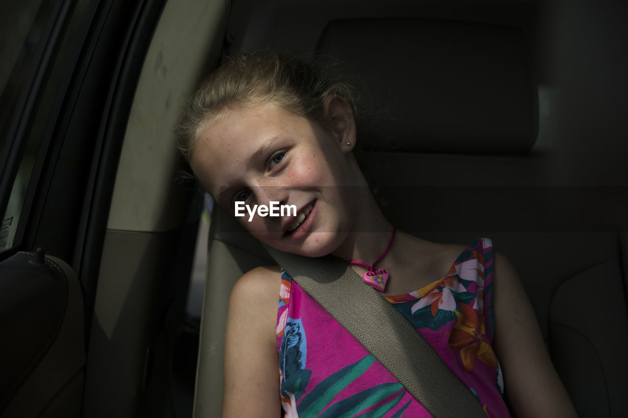 Young smiling blonde girl sits in back seat of car, window light