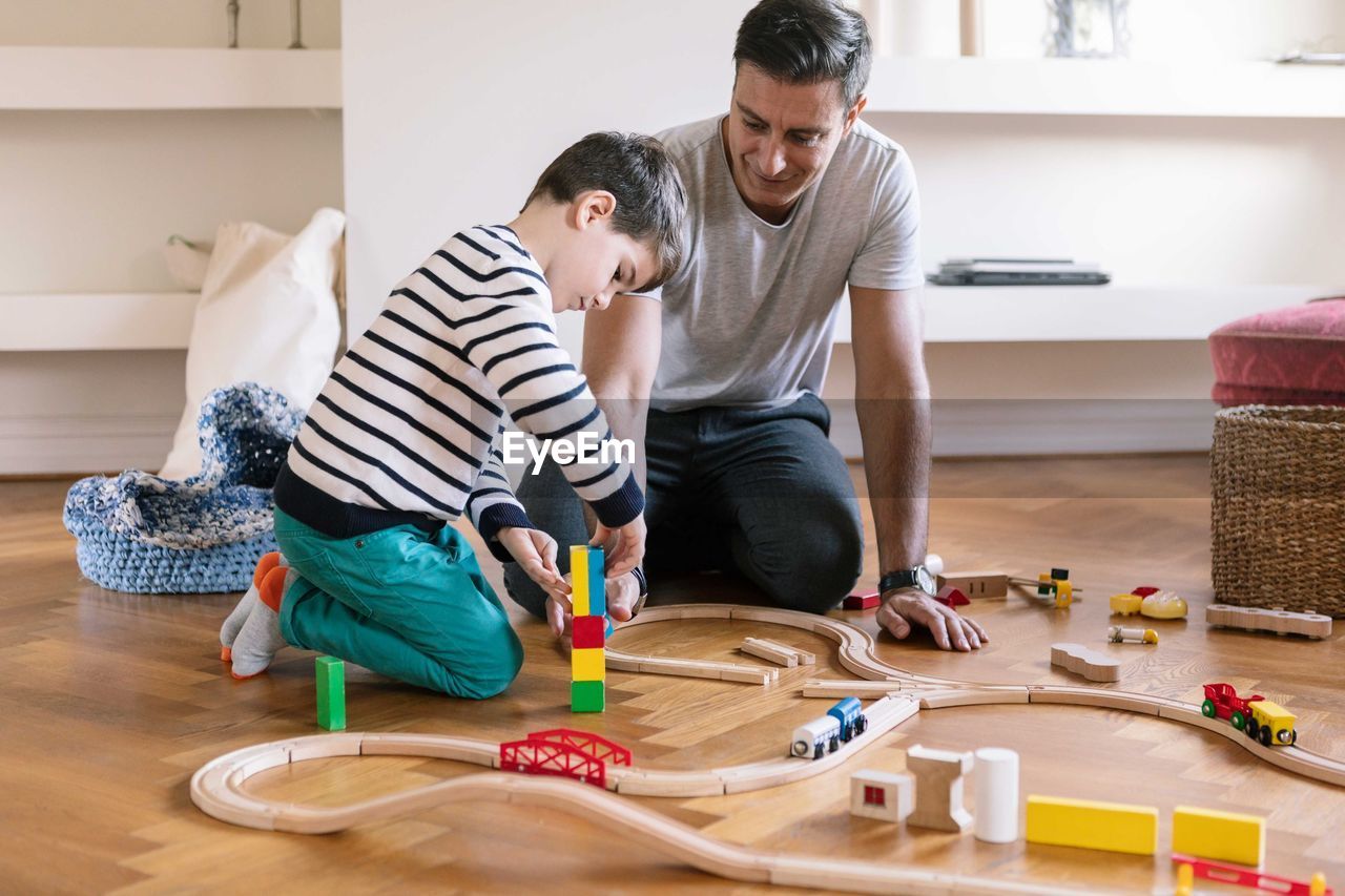 Smiling father playing with son while kneeling in living room