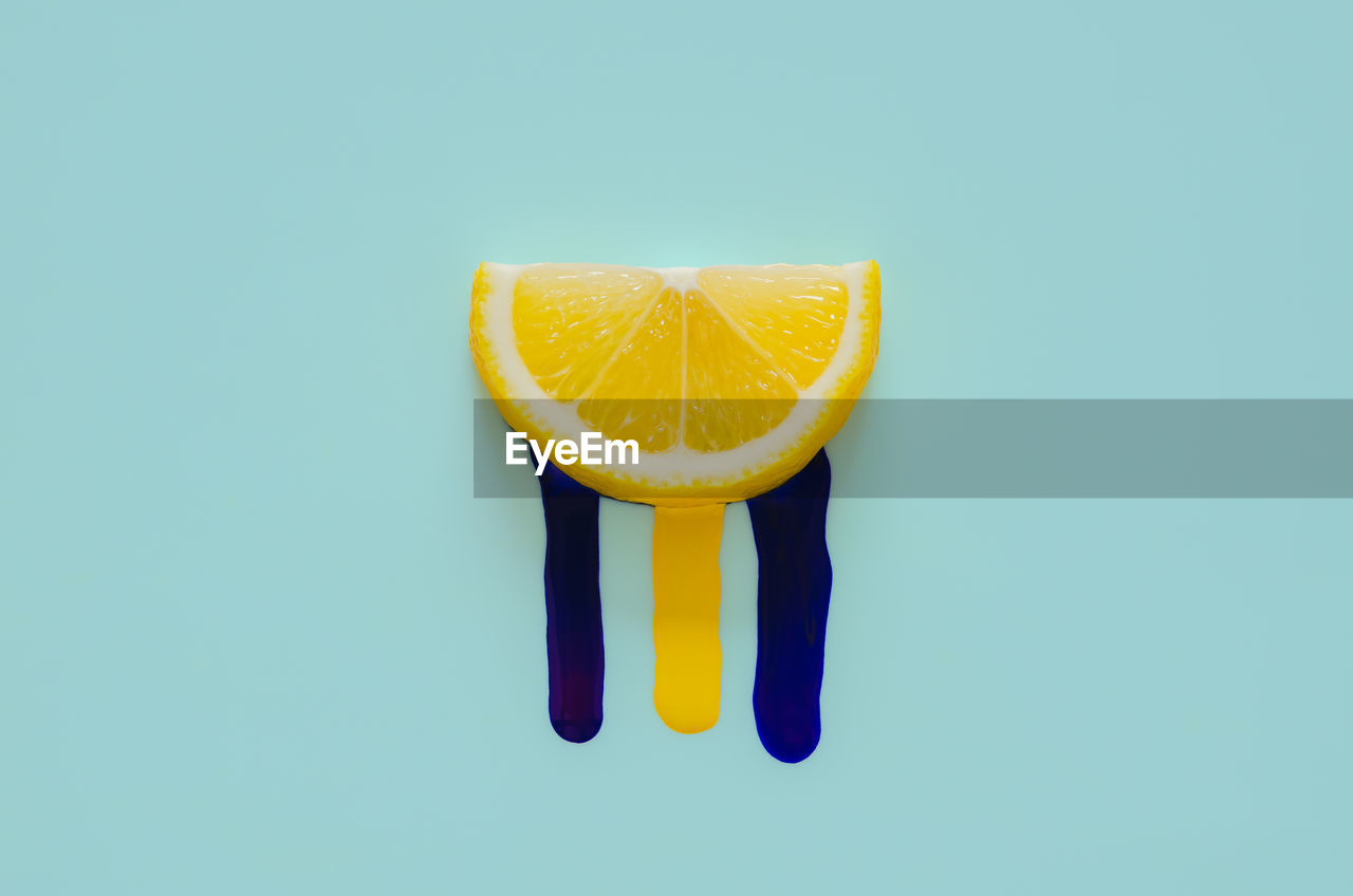 Slice lemon that have poster color drop from it with blue background. minimal summer concept.