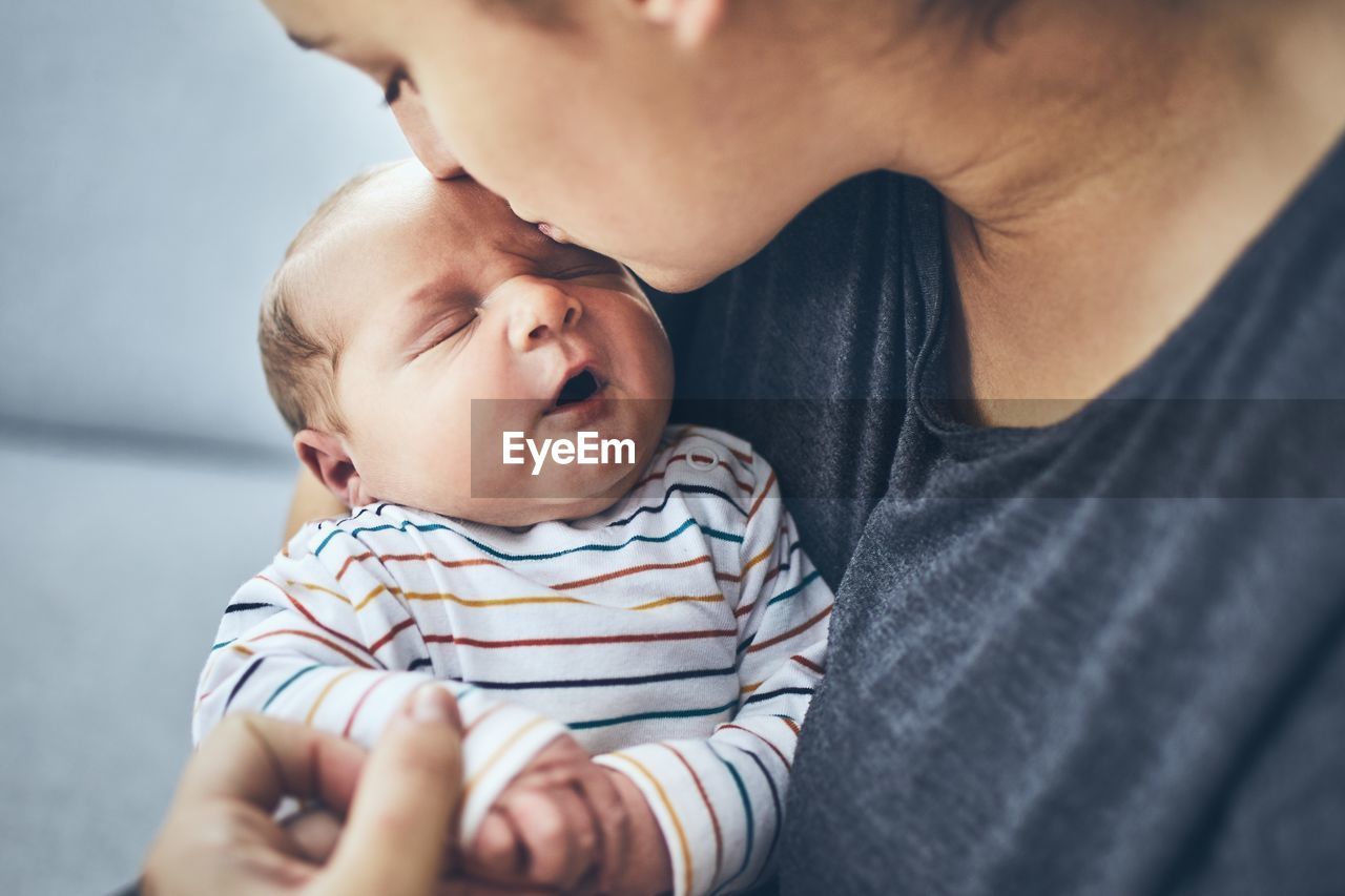 Close-up of woman kissing newborn son while sitting on sofa at home