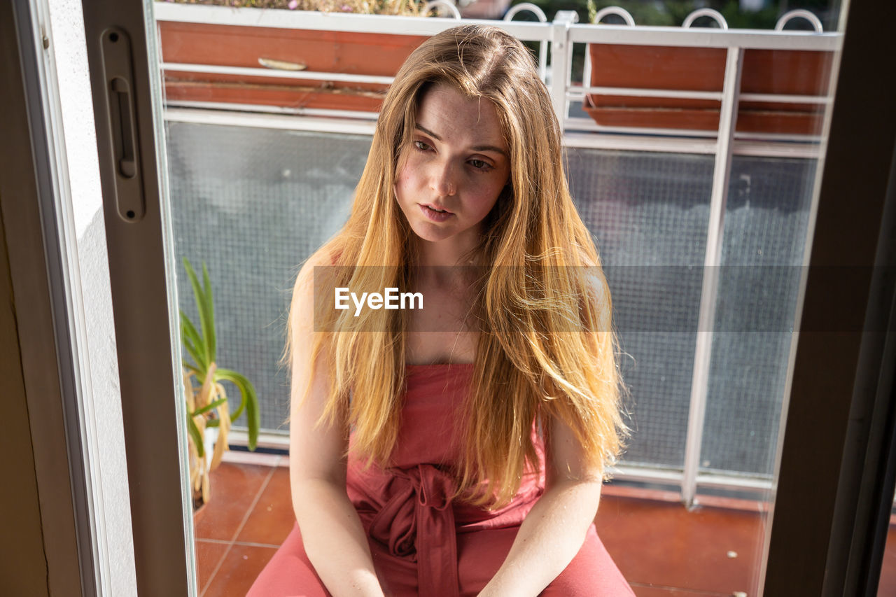 PORTRAIT OF YOUNG WOMAN LOOKING AT WINDOW AT HOME