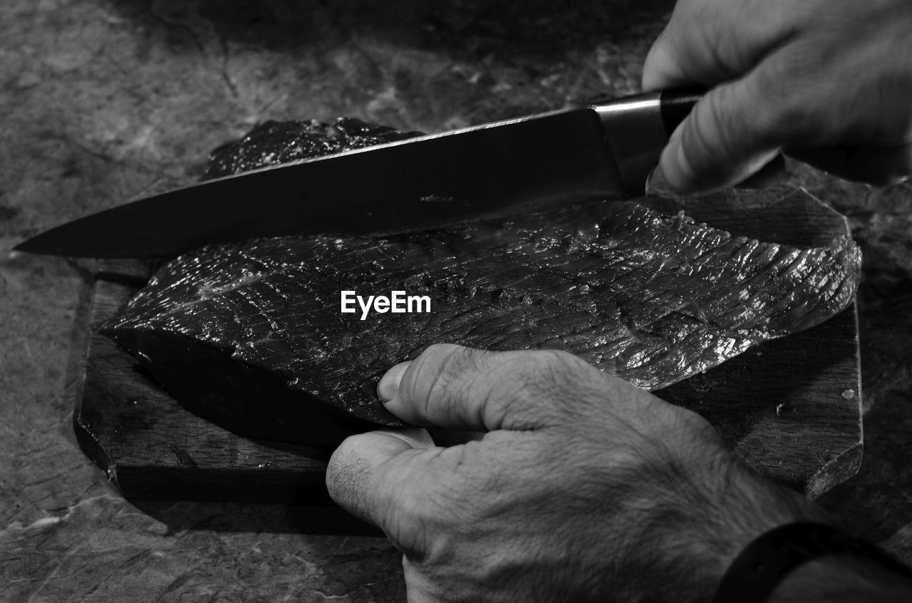 Cropped hands of man cutting meat on table