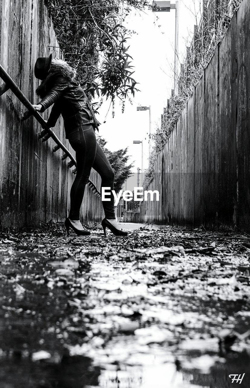 Side view full length of woman standing by wall on alley