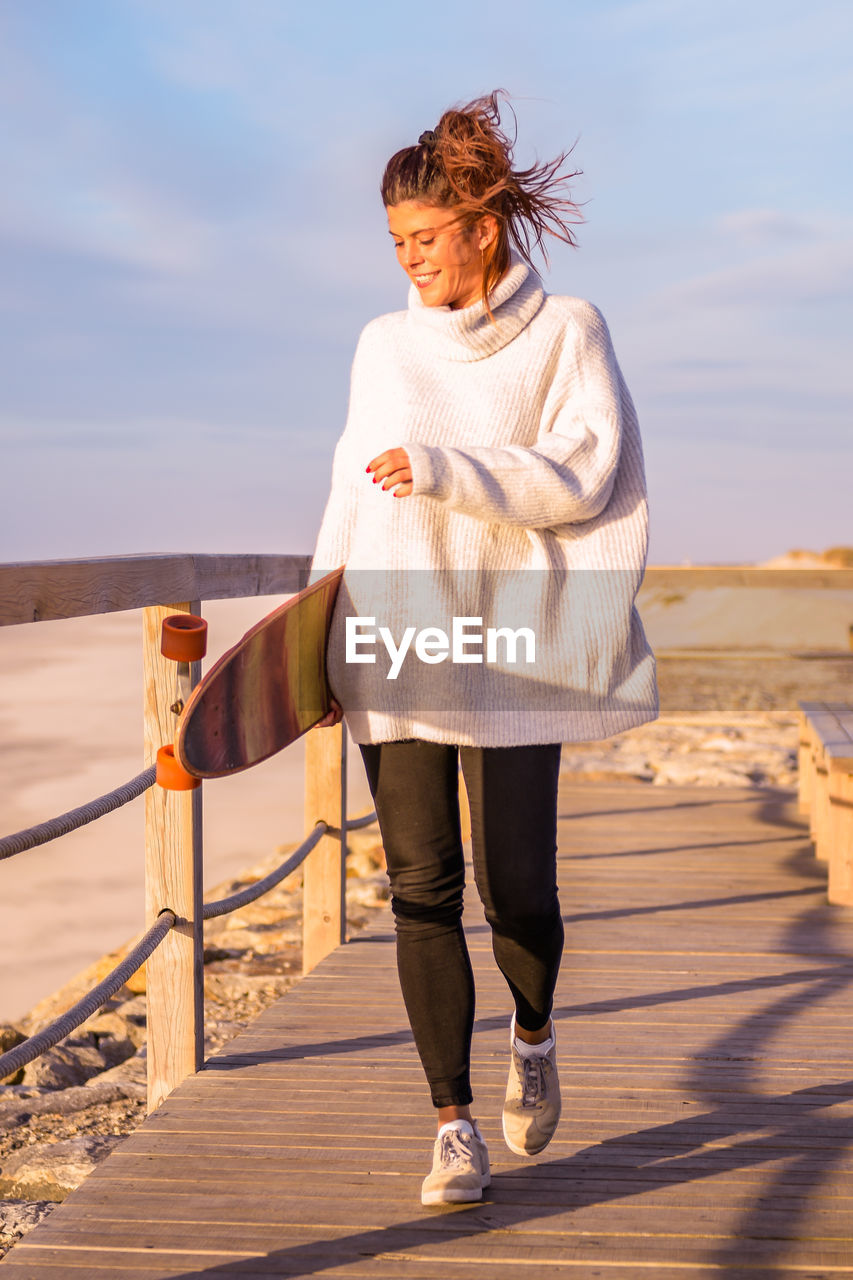 full length of young woman walking on beach against sky