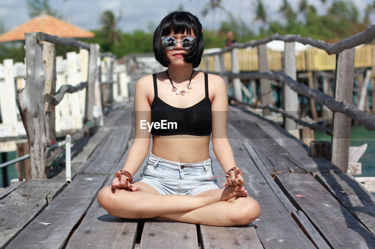 Portrait of woman doing while sitting on wooden bridge