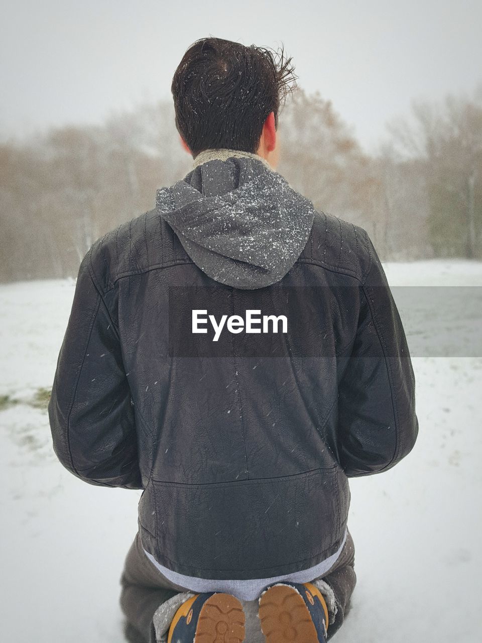 Rear view of man wearing hood while sitting on snow field