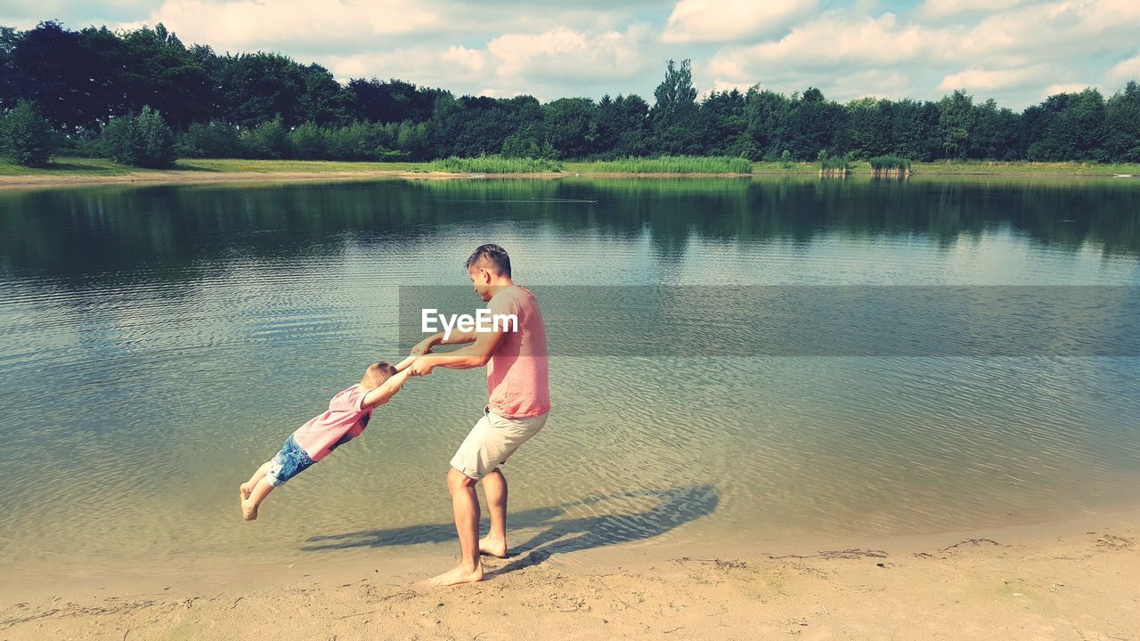 Side view of father and son playing at lakeshore