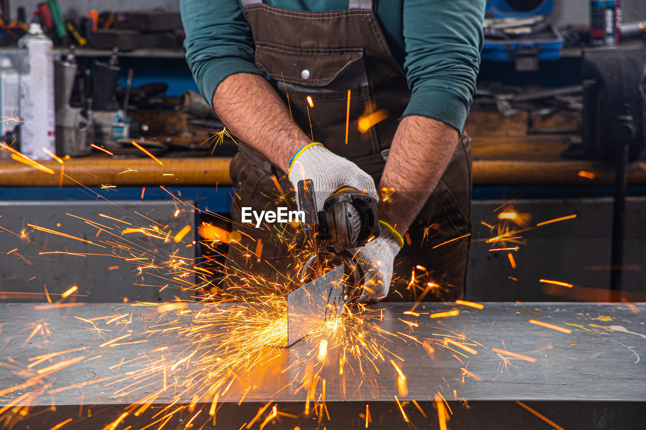 . a young male welder grinds a metal product with angle grinder in the garage