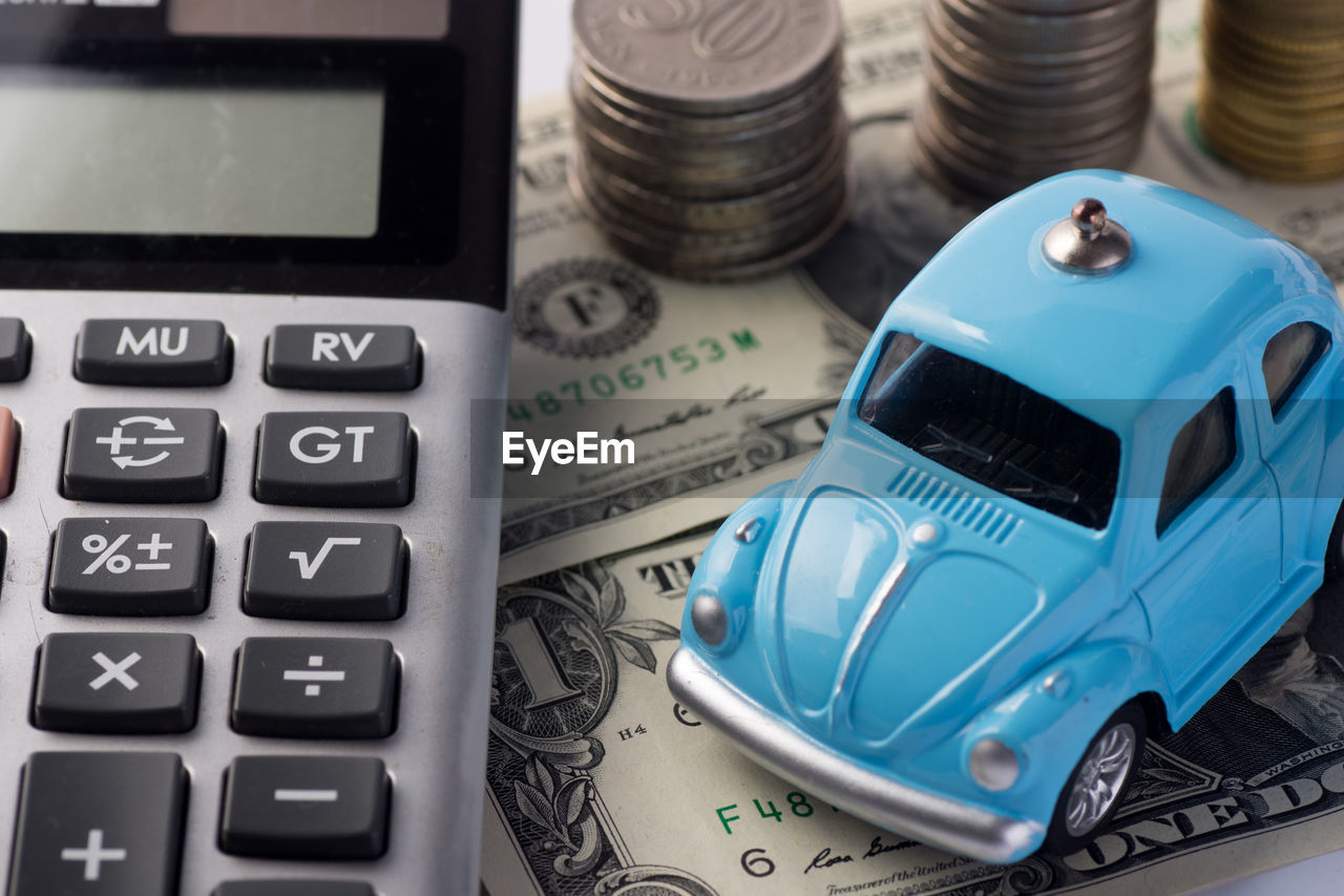 Close-up of toy car by calculator and currency against white background