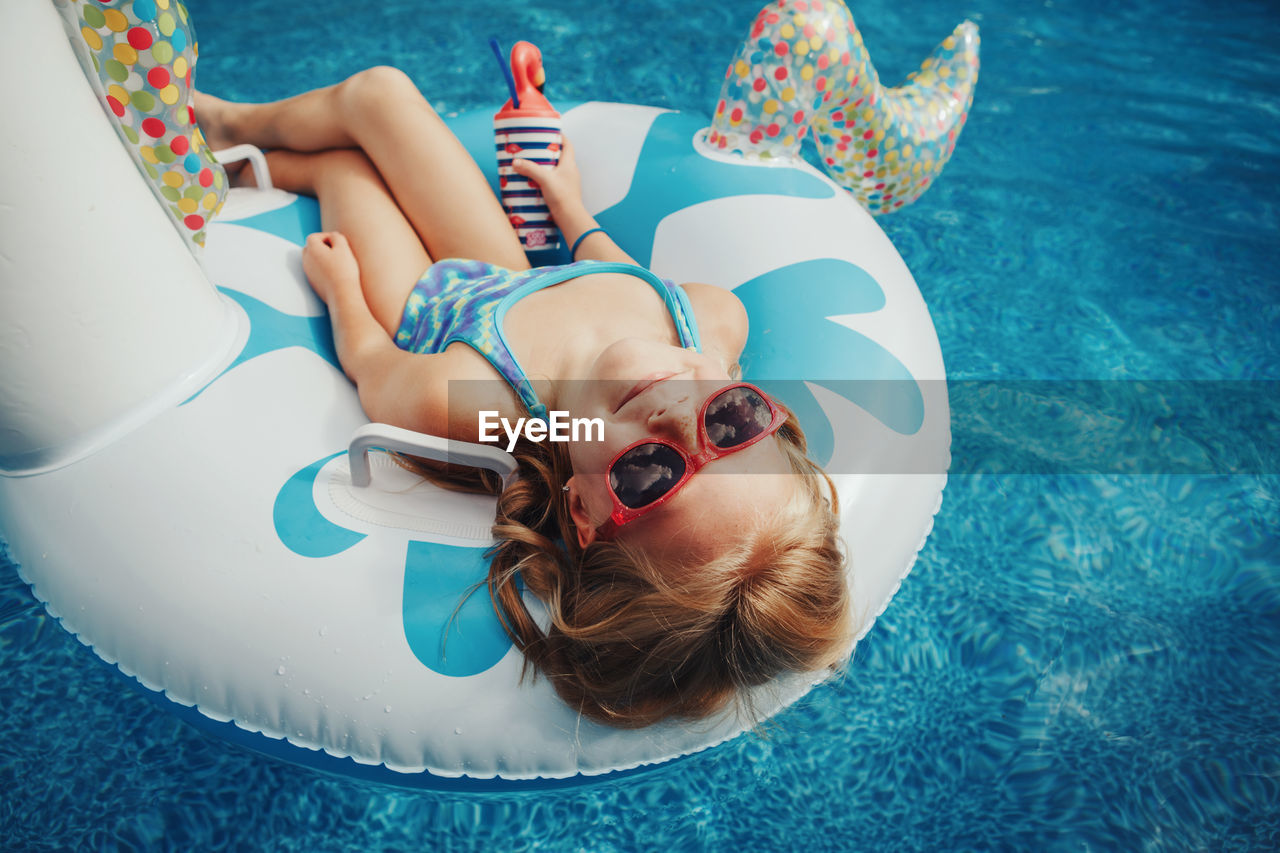 Cute adorable girl in sunglasses with drink lying on inflatable ring unicorn. kid child enjoying 