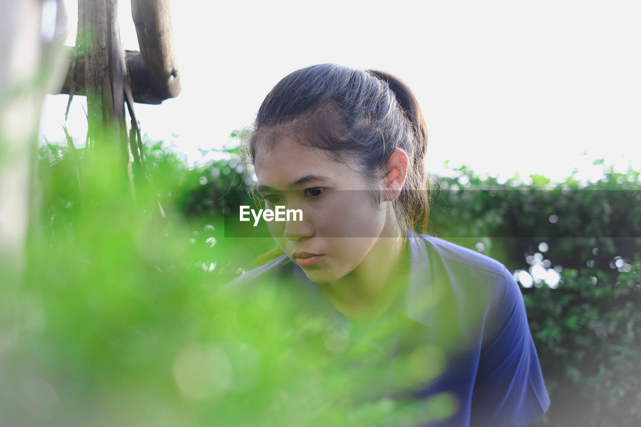 Young woman looking away while standing against clear sky