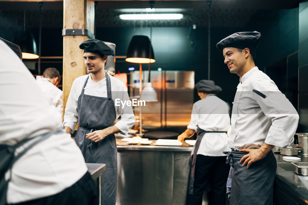 Men in hats and aprons working in team and serving dishes with delicious food in kitchen