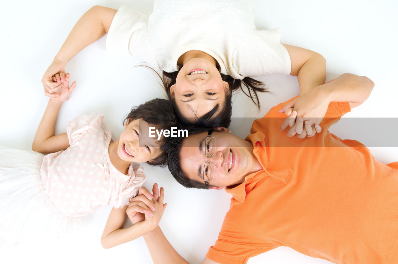 Directly above portrait of smiling parents lying down with daughter on bed at home