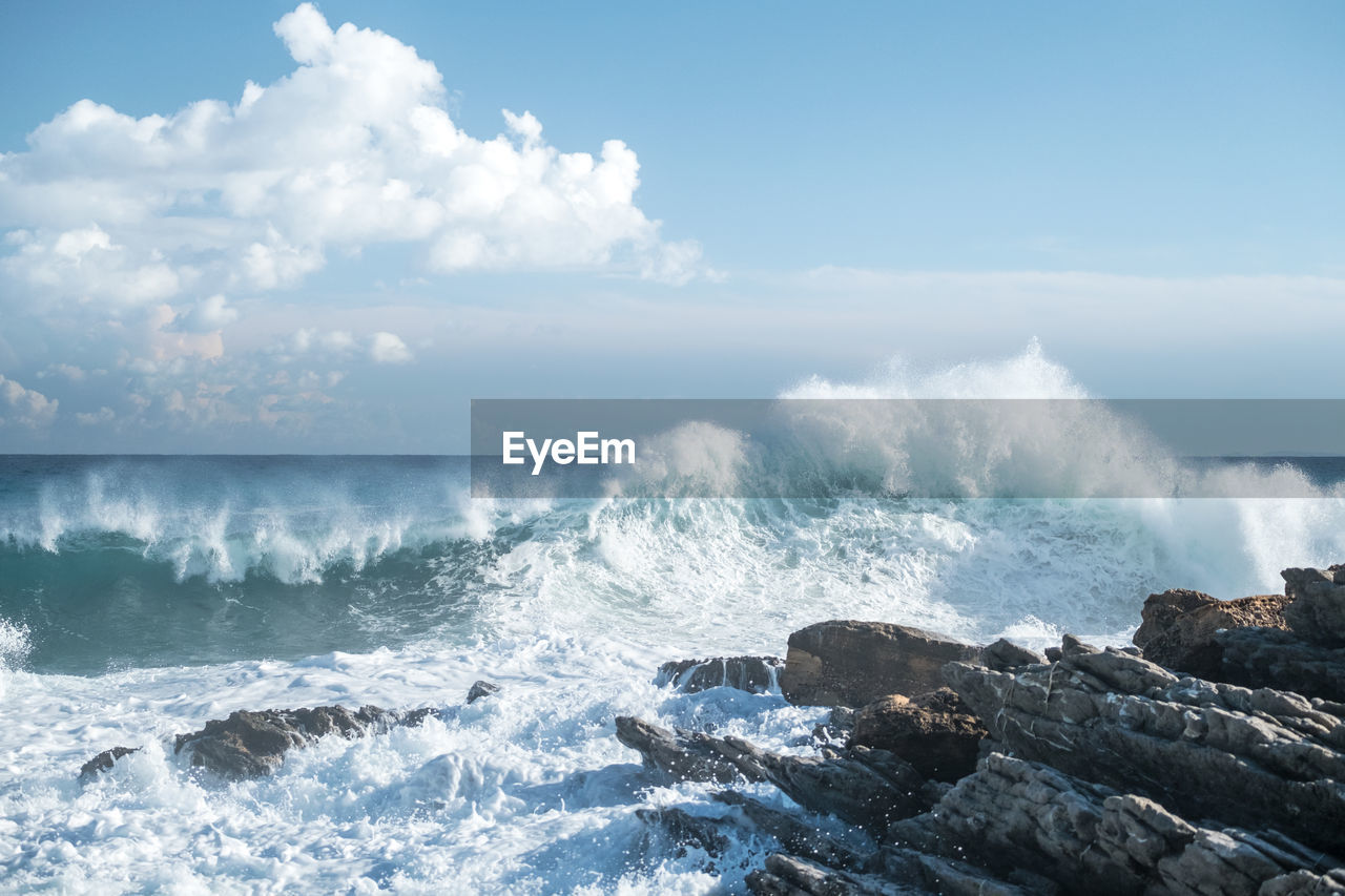 Waves crashing on rock against cloudy sky