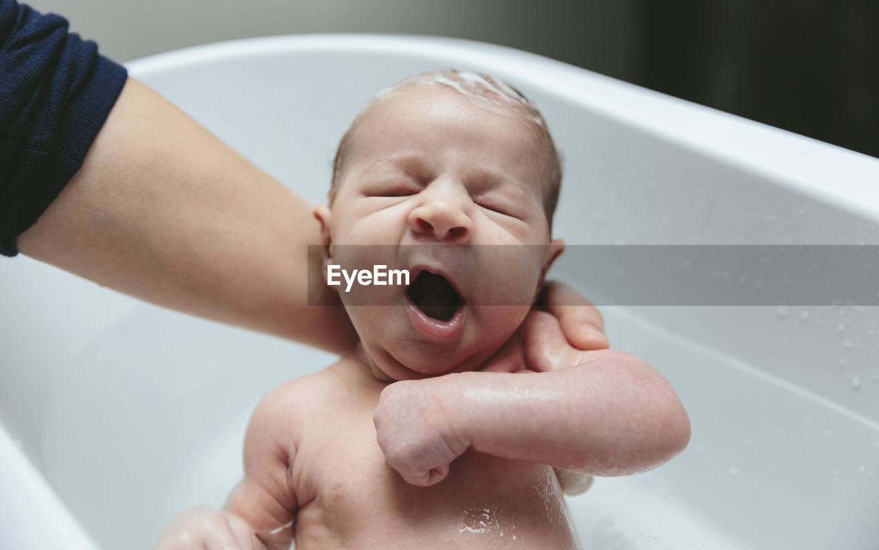 Cropped hands of mother bathing son in bathtub at bathroom