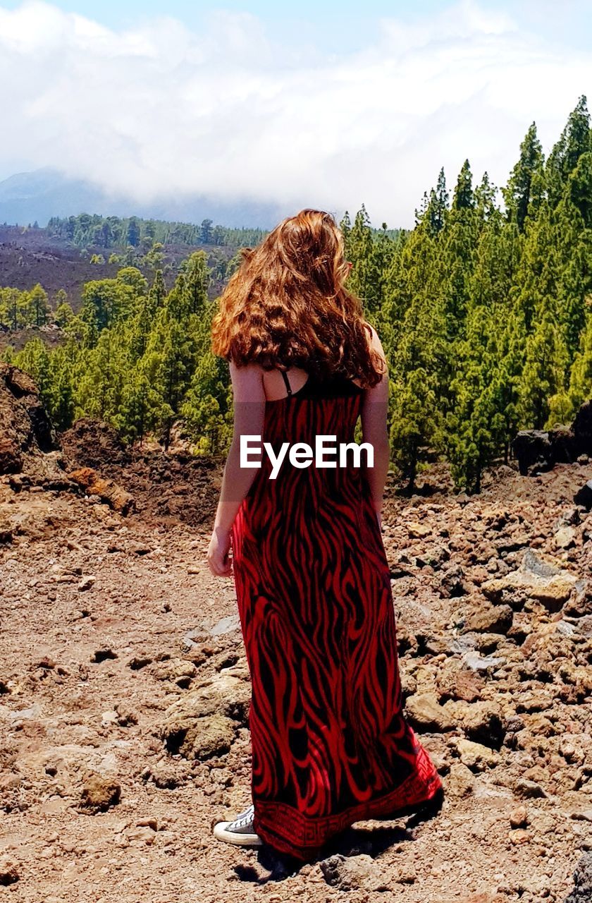 Rear view of teenage girl standing on field against sky