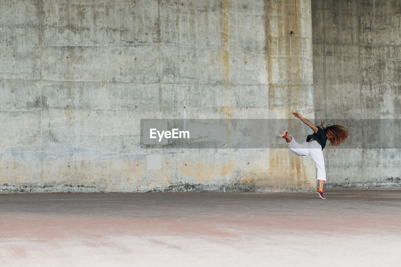 Young woman doing acrobatic jump while exercising against wall