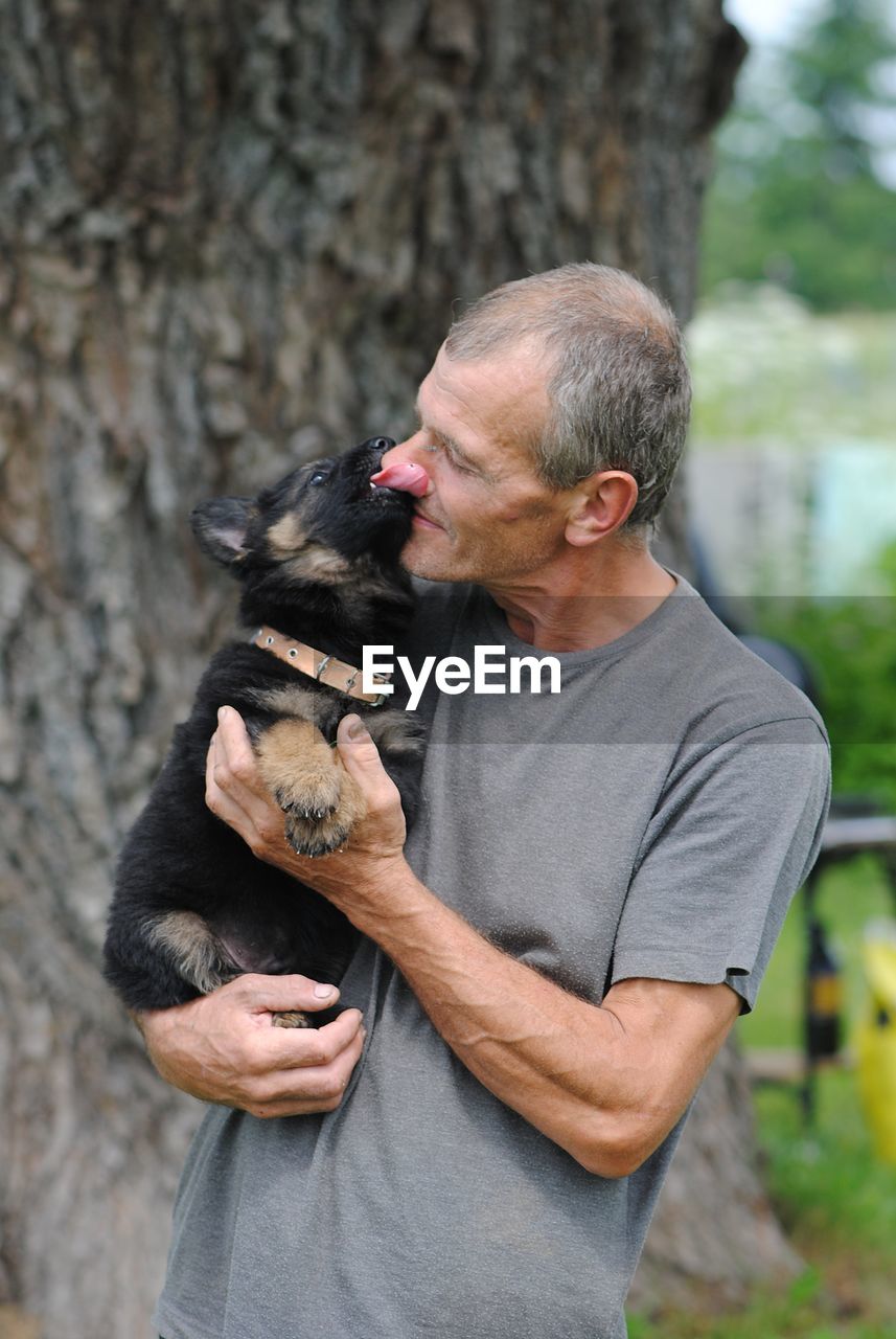 Man carrying puppy by tree