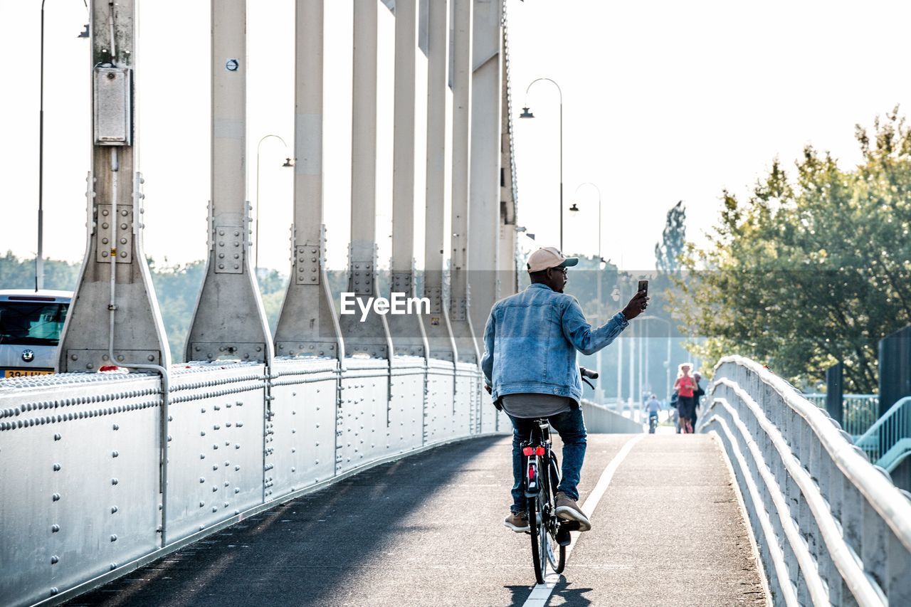 Rear view of man riding bicycle on bridge in city