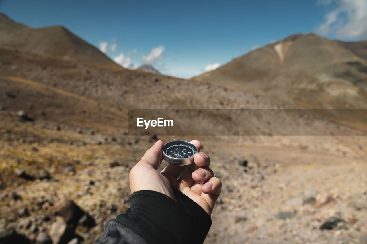 First-person view of a male traveler's hand holding a magnetic compass against the backdrop 