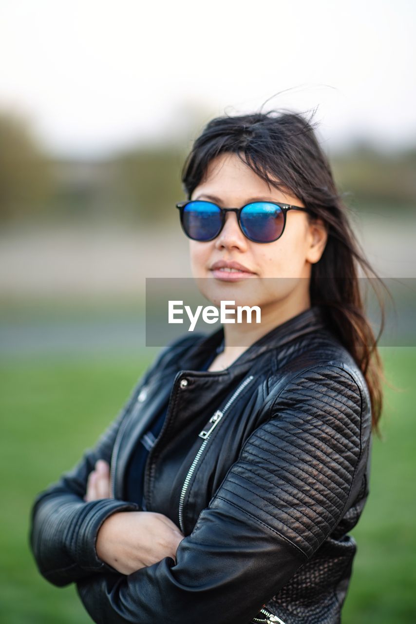 PORTRAIT OF BEAUTIFUL YOUNG WOMAN WEARING SUNGLASSES STANDING ON FIELD