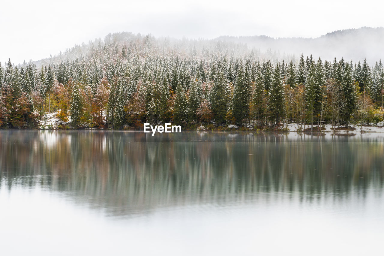 Between autumn and winter. warm and cold reflections of snow on lake fusine.