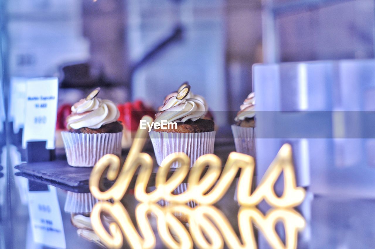 Close-up of cupcakes with cheers sign reflected in foreground 
