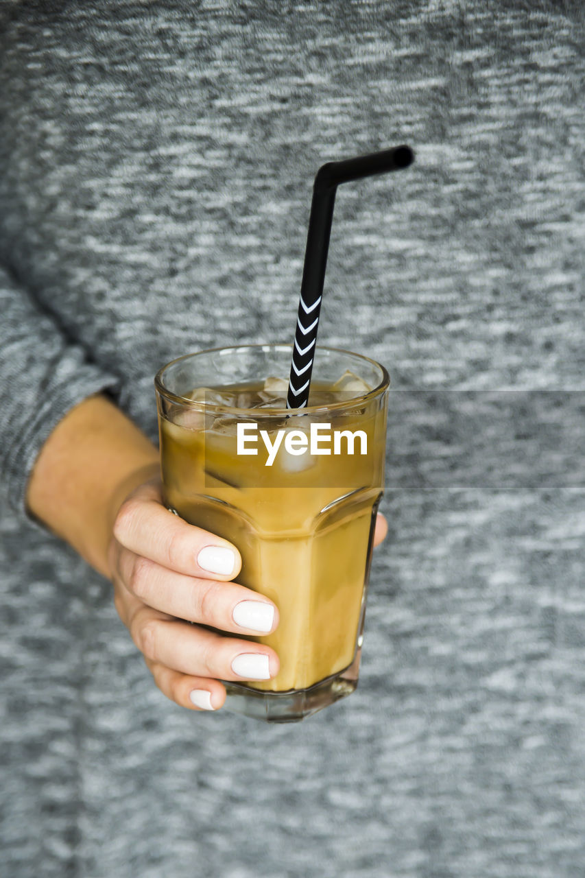 Close-up of hand holding drinking straw in cold coffee on table