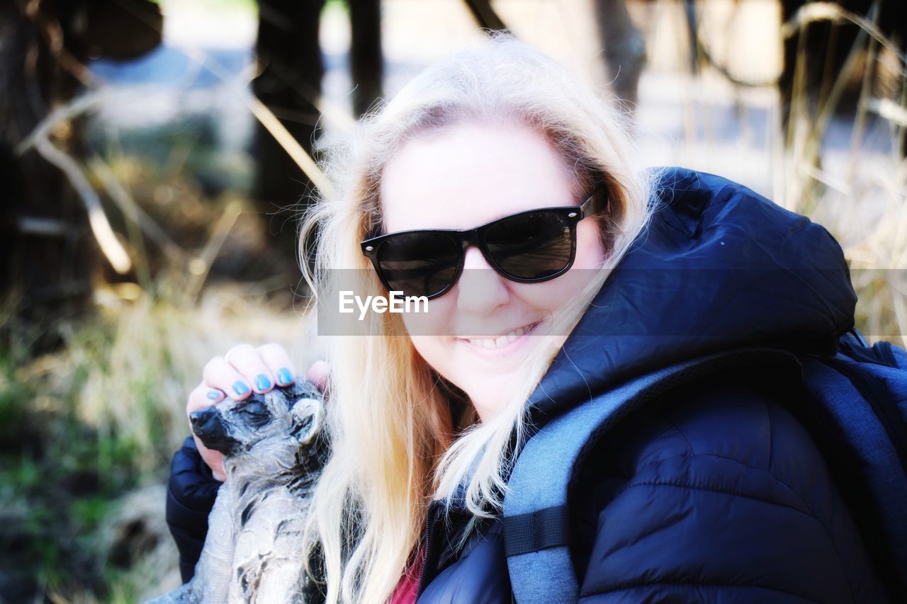 PORTRAIT OF SMILING WOMAN WEARING SUNGLASSES OUTDOORS