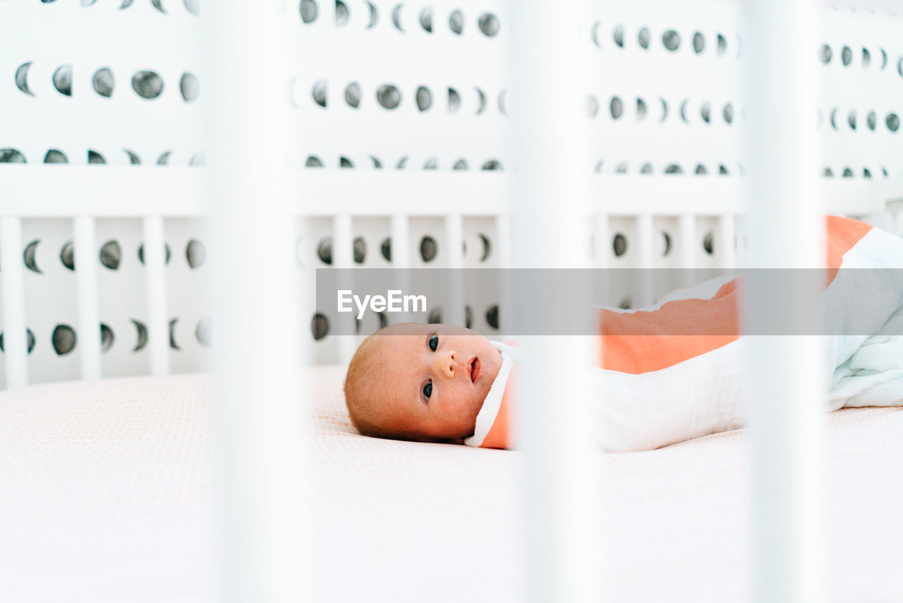 View through a crib of a newborn baby girl laying down