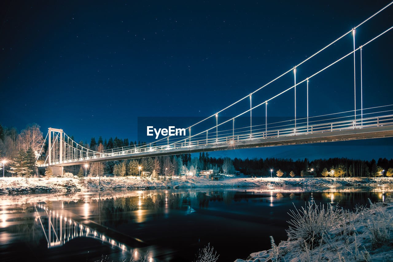 Illuminated bridge over river against sky at night