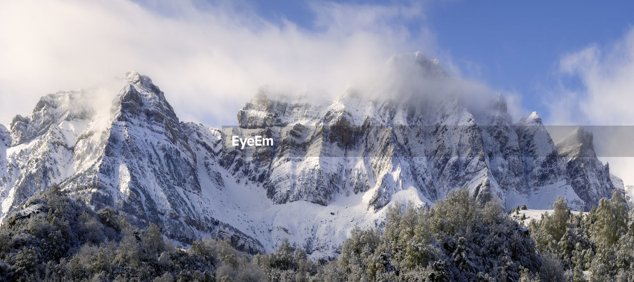 Clouds between mountains in a panoramic snowy landscape at winter
