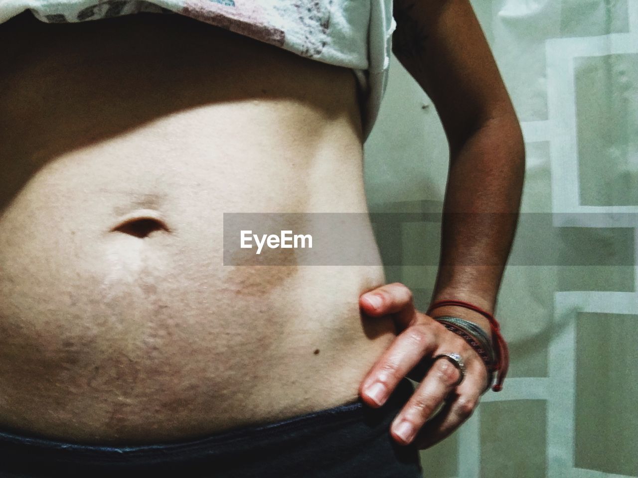 MIDSECTION OF WOMAN HOLDING HANDS WHILE STANDING IN KITCHEN