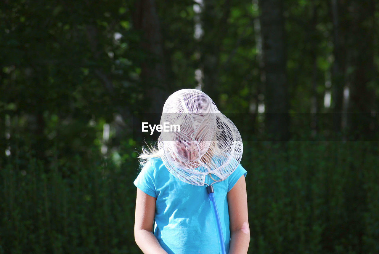 Girl wearing butterfly net on face while standing in forest