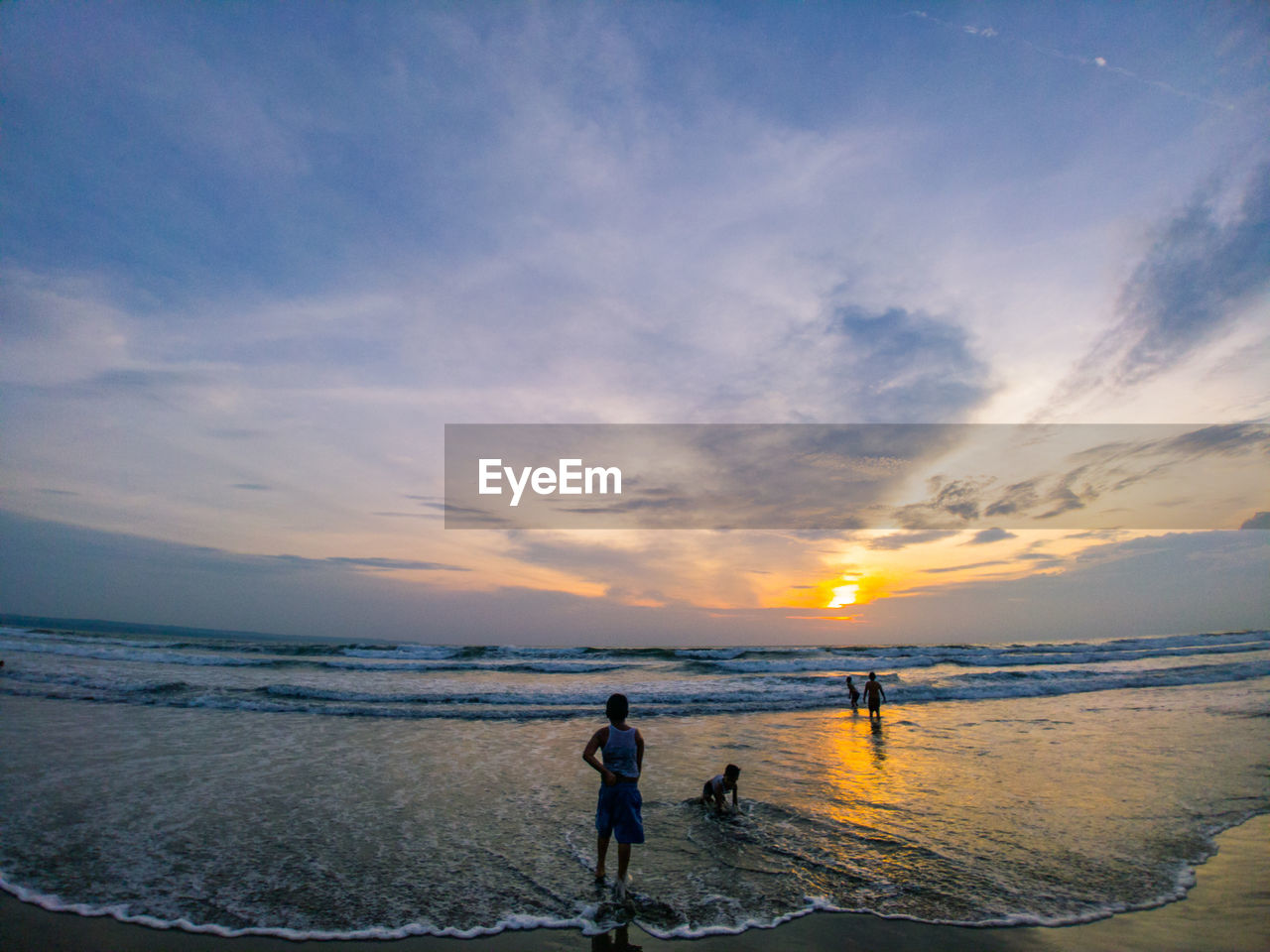 SILHOUETTE MAN STANDING ON BEACH AGAINST SKY AT SUNSET