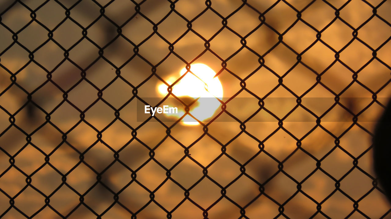 CLOSE-UP OF CHAINLINK FENCE AGAINST SUNSET