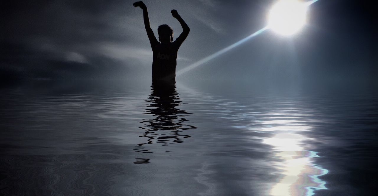 Silhouette boy exploring in sea on sunny day