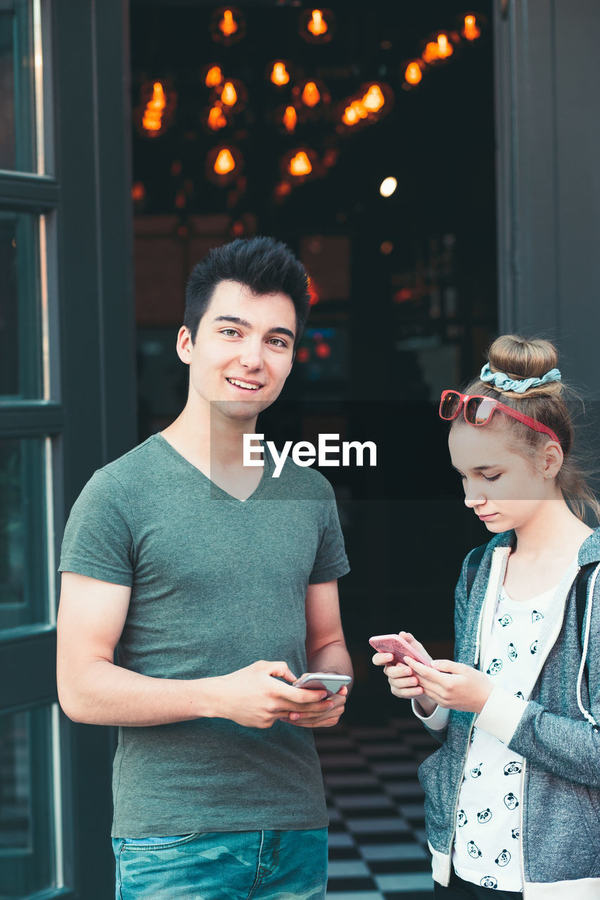 Smiling teenage friends using mobile phone in city